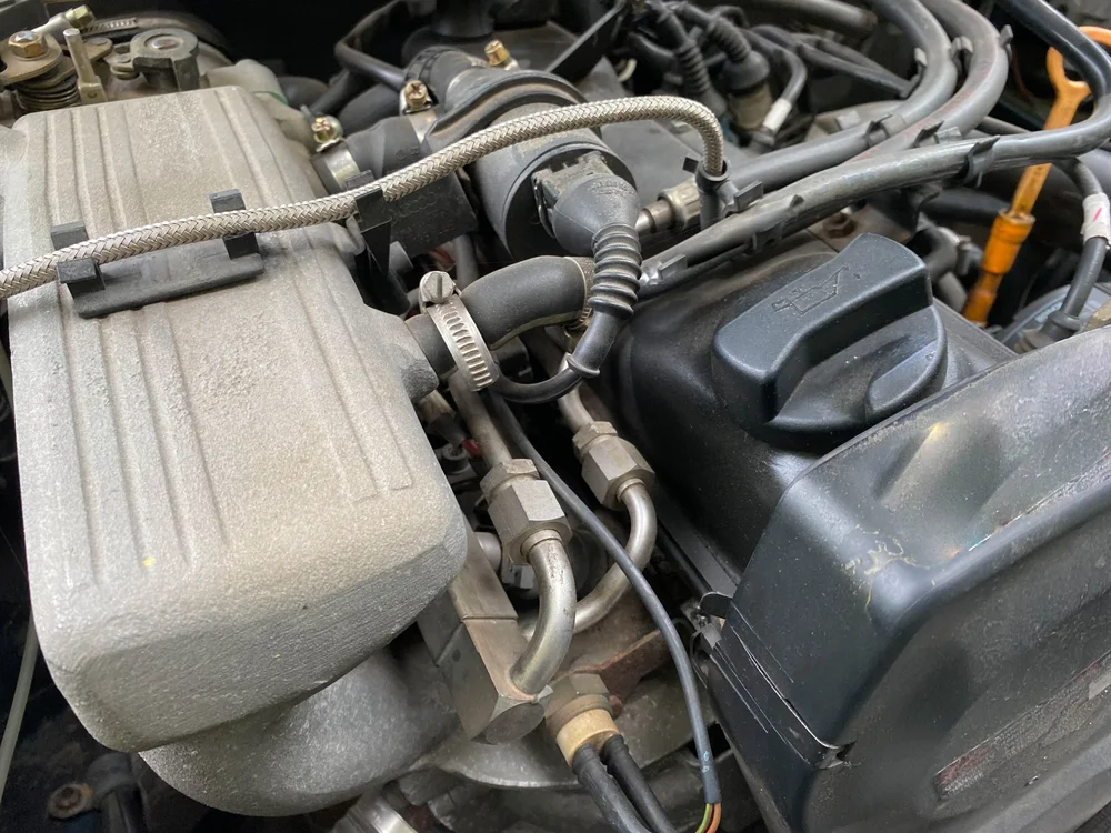 Close-up under the hood showing engine bay hoses, fittings and fluid reservoir