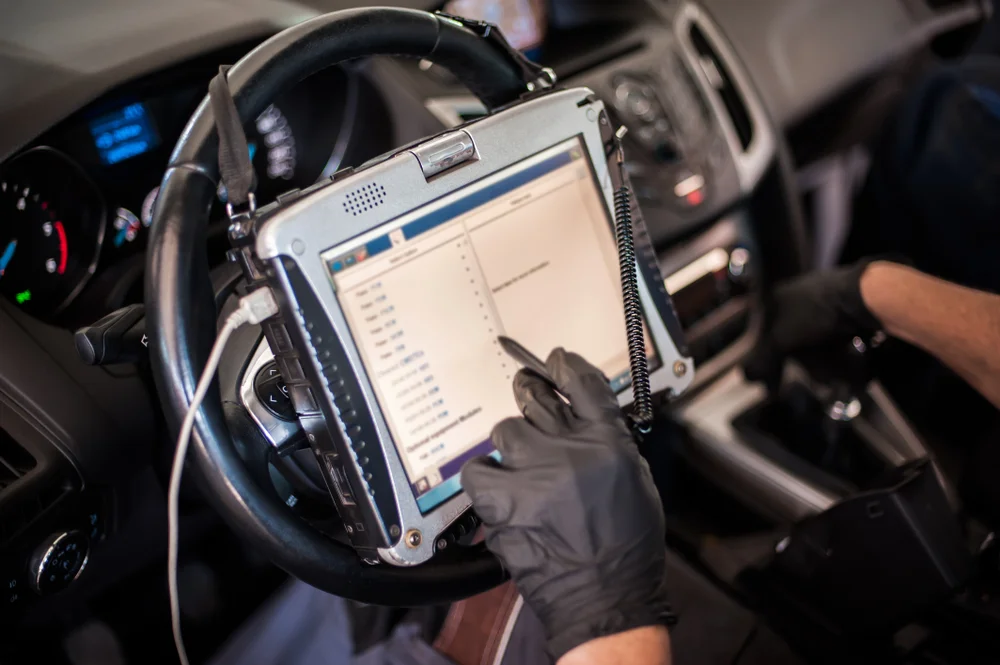 Technician using a tablet-style diagnostic scan tool mounted on the steering wheel, reviewing vehicle data